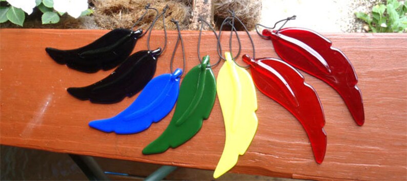 Puede incluir: Seis adornos de plumas de vidrio en varios colores, incluyendo negro, azul, verde, amarillo y rojo. Las plumas cuelgan de cuerdas.