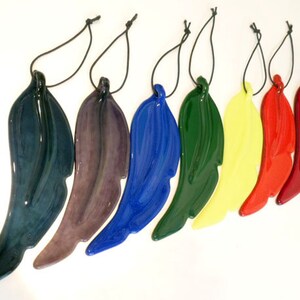 Puede incluir: Siete adornos de plumas de vidrio en varios colores, incluyendo azul, verde, morado, rojo y amarillo. Cada pluma est&aacute; unida a una cuerda negra para colgar.
