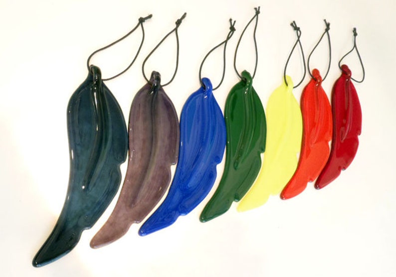 Puede incluir: Siete adornos de plumas de vidrio en varios colores, incluyendo azul, verde, morado, rojo y amarillo. Cada pluma est&aacute; unida a una cuerda negra para colgar.