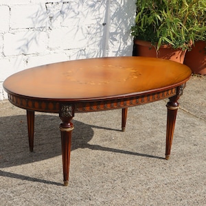 Può includere: Un tavolino da caffè ovale in legno con un design a intarsio. Il tavolo ha quattro gambe con accenti dorati e una finitura marrone scuro.