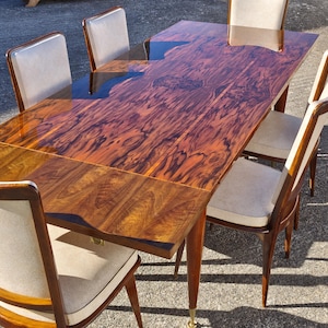 Peut inclure: Une table à manger rectangulaire avec une finition en bois brun foncé très brillante et un ensemble de chaises assorties. Chaque chaise présente un cadre en bois et une assise rembourrée de couleur claire. La surface de la table montre un motif tourbillonnant.