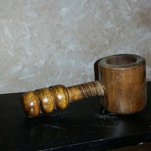 May include: A wooden nutcracker with a brown finish. The nutcracker has a threaded handle and a round, open top for cracking nuts.