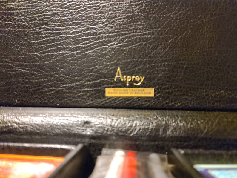 Op de afbeelding: Een zwarte leren doos met een gouden label waarop staat "Asprey, English Leather, Made in England."