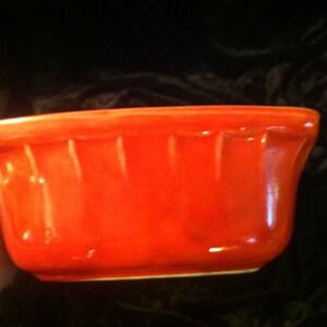 May include: A bright orange ceramic bowl with a fluted rim. The bowl is empty and has a glossy finish.