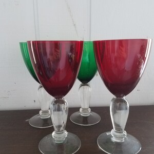 May include: Set of four wine glasses with clear stems and bases. Two glasses are red and two are green.