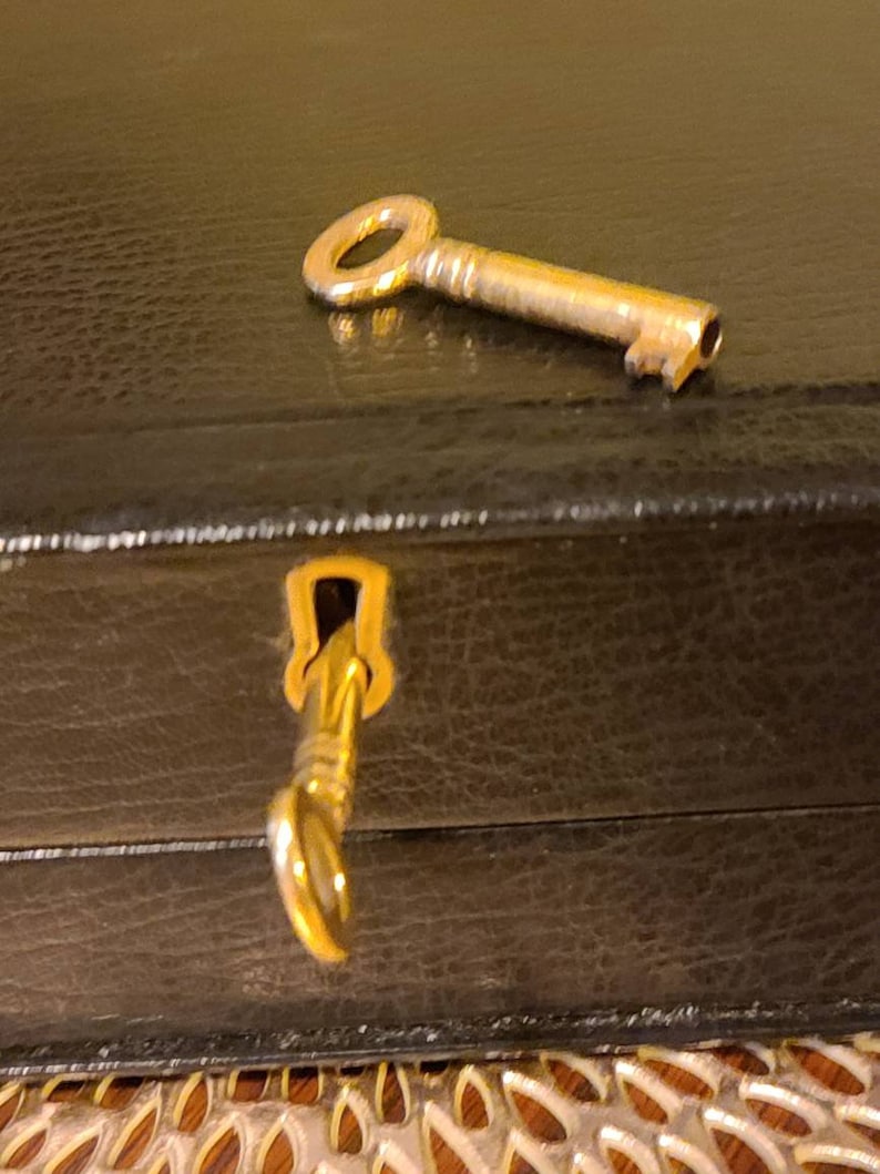Op de afbeelding: Een gouden sleutel met een rond sleutelgat ligt op een zwarte lederen doos. De sleutel is gedeeltelijk in het sleutelgat van de doos gestoken.