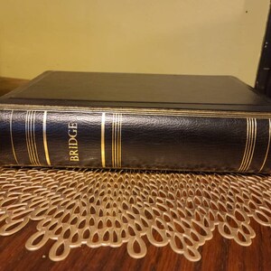 Op de afbeelding: Een zwart lederen gebonden boek met gouden accenten en het woord "BRIDGE" gegraveerd op de rug.