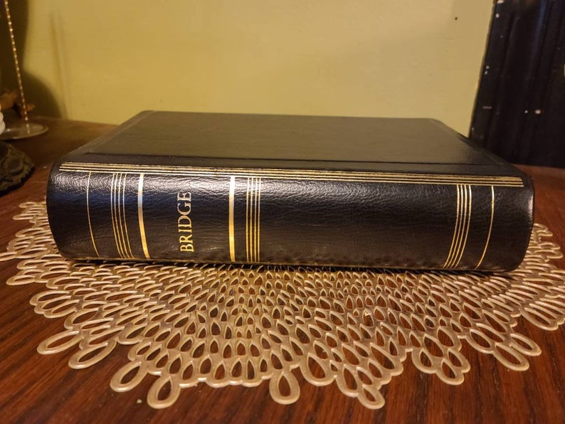 Op de afbeelding: Een zwart lederen gebonden boek met gouden accenten en het woord "BRIDGE" gegraveerd op de rug.
