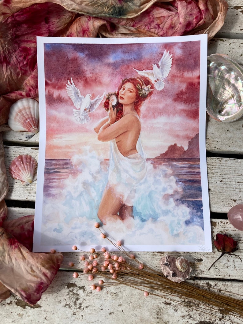 May include: A watercolor painting of a woman with red hair standing in the ocean waves. She is holding a seashell and two white doves are flying around her. The background is a sunset sky with pink and purple clouds.