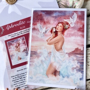 May include: Aphrodite, the Greek goddess of love and beauty, is depicted in a watercolor painting. She is standing in the ocean waves, holding a mirror and surrounded by white doves. The painting has a pink and orange sunset sky in the background.