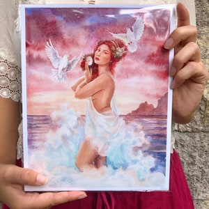 May include: A watercolor painting of a woman standing in the ocean with two white doves flying above her. She is holding a mirror in her left hand and a wreath of flowers in her right hand. The background is a sunset sky with pink and orange clouds.
