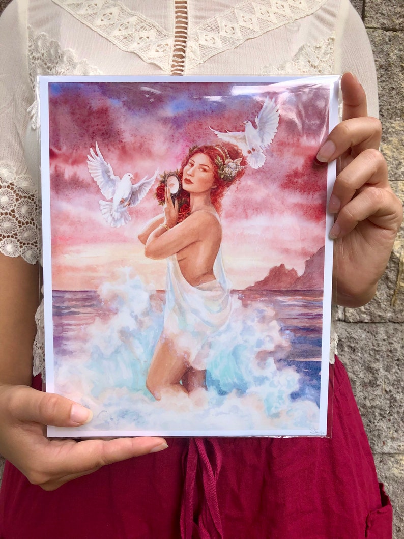 May include: A watercolor painting of a woman standing in the ocean with two white doves flying above her. She is holding a mirror in her left hand and a wreath of flowers in her right hand. The background is a sunset sky with pink and orange clouds.