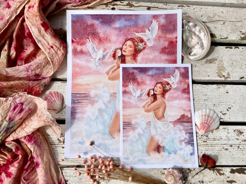 May include: Two watercolor prints of a woman with flowing white fabric and doves flying above her. The woman is holding a seashell to her ear. The background is a sunset over the ocean.
