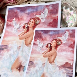 May include: A watercolor painting of a woman with red hair and a white dress standing in the ocean with doves flying around her. The background is a sunset with pink, purple, and orange colors.