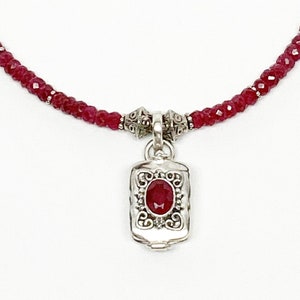 May include: A red ruby gemstone necklace with a silver pendant featuring a ruby gemstone. The pendant has an ornate design.