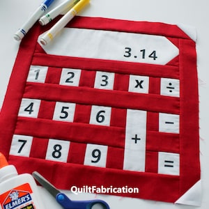May include: A red and white fabric calculator with black numbers and symbols. The calculator has a white label at the top with the number 3.14 written on it.
