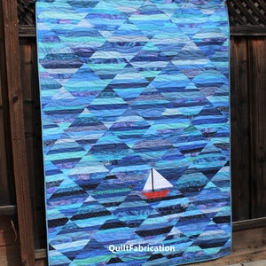 May include: A blue and white quilt with a sailboat design. The quilt is made of many different shades of blue and white fabric, and the sailboat is a bright red with a white sail. The quilt is hanging on a wooden fence. The text "QuiltFabrication" is visible in the bottom right corner of the quilt.