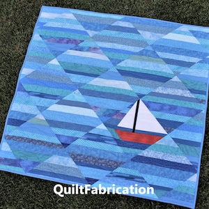 May include: A blue and white quilt with a red and white sailboat in the center. The quilt is made of various shades of blue fabric and has a diamond pattern. The text "QuiltFabrication" is printed in the bottom right corner.