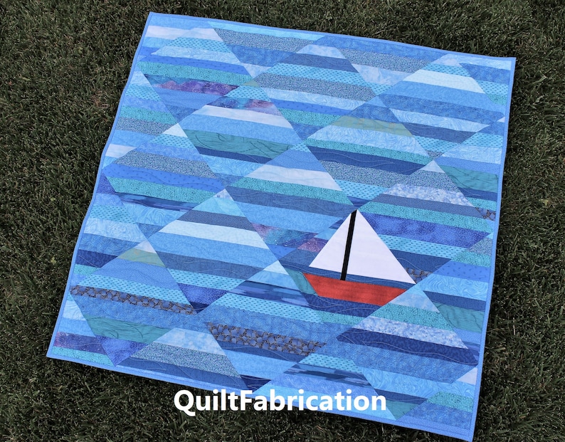 May include: A blue and white quilt with a red and white sailboat in the center. The quilt is made of various shades of blue fabric and has a diamond pattern. The text "QuiltFabrication" is printed in the bottom right corner.