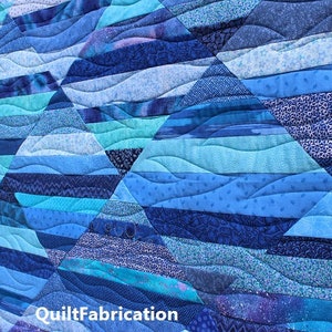 May include: A blue and teal quilt with a wavy pattern. The quilt is made of different fabrics with various shades of blue and teal. The quilt is quilted with a wavy pattern, creating a sense of movement and depth. The quilt is signed "QuiltFabrication" in the bottom right corner.