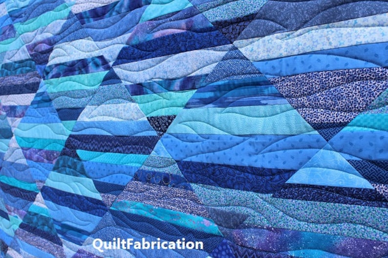 May include: A blue and teal quilt with a wavy pattern. The quilt is made of different fabrics with various shades of blue and teal. The quilt is quilted with a wavy pattern, creating a sense of movement and depth. The quilt is signed "QuiltFabrication" in the bottom right corner.