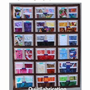 Op de afbeelding: Een gewatteerde wandhanger met meerdere stoffen opbergvakken. Elk vak heeft een andere kleur en patroon, met een bruine rand en de tekst "Scrap Storage by QuiltFabrication" bovenaan en onderaan.