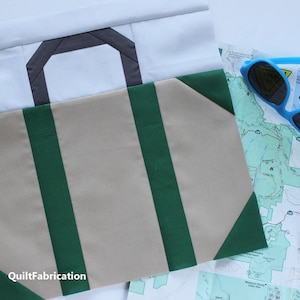 May include: A beige and green fabric block with a gray fabric handle. The block is a quilt square and is part of a larger quilt project. The text "QuiltFabrication" is visible in the bottom left corner of the image.