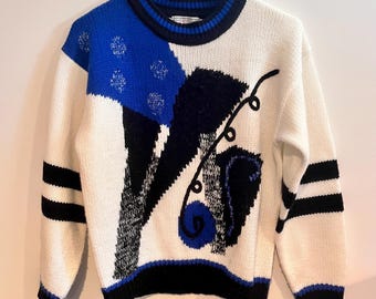 May include: A white sweater with a bold, abstract design. The sweater features a blue and black color block pattern on the front, with black stripes on the sleeves. The collar and cuffs are trimmed in black and blue.