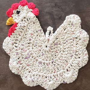 May include: A crocheted white chicken dishcloth with a red and yellow head. The dishcloth is made with a variety of stitches and has a scalloped edge.