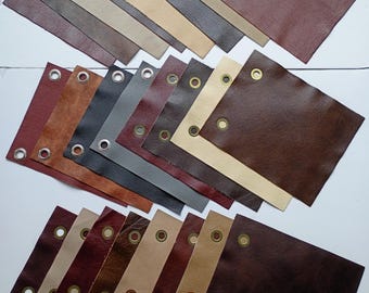 Può includere: Assortimento di campioni di pelle in varie tonalità di marrone, beige e grigio. Ogni campione ha un occhiello dorato nell'angolo. I campioni sono disposti in tre file, mostrando i diversi colori e le trame della pelle.