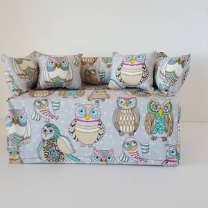 May include: A gray tissue box cover with a white background and a pattern of colorful owls. The cover has four pillows with owl designs on them.