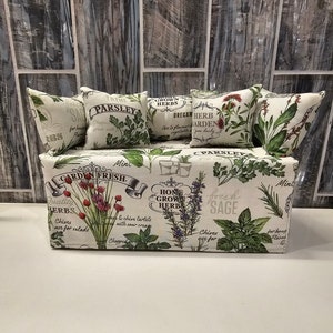 Może przedstawiać: Biała kanapa z tkaniny z kwiatowym wzorem przedstawiającym różne zioła i przyprawy. Kanapa ma pięć poduszek z różnymi wzorami ziół, w tym pietruszką, tymiankiem, oregano i szałwią. Tekst na poduszkach i kanapie brzmi "Garden Fresh", "Home Grown Herb", "Parsley", "Thyme", "Crown Grown Herbs", "Oregano", "Herb Garden" i "Fresh Sage".