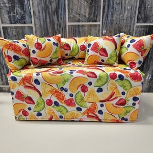 Op de afbeelding: Een witte tissueboxhoes met een kleurrijke fruitprint. De hoes heeft een verscheidenheid aan fruit, waaronder perziken, citroenen, limoenen, kersen en blauwe bessen. De hoes is versierd met vier kleine kussens, elk met dezelfde fruitprint.