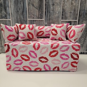 Puede incluir: Una funda para caja de pañuelos blanca con un diseño de estampado de labios rosa y rojo. La funda tiene cuatro almohadas a juego con el mismo diseño de estampado de labios.