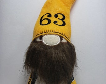 May include: A yellow and black gnome with a brown beard. The gnome is wearing a yellow hat with the number 63 on it. The gnome is also wearing a black and yellow fabric with the Boston Bruins logo and the NHL logo.