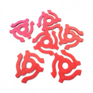 May include: Five bright red, star-shaped vinyl record adapters, each featuring a central circular hole and three curved, radiating arms. These plastic inserts are arranged in a loose, circular pattern against a plain white background.