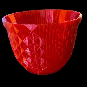 May include: A vibrant red planter featuring a distinct geometric diamond pattern across its exterior surface. The bowl-shaped container has a wide, open top and a smooth, rounded rim, showcasing a textured, faceted design that catches the light.