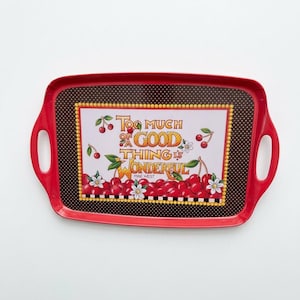 May include: A rectangular red serving tray with integrated handles. The center features a dark brown background with white polka dots, a yellow beaded border, and a graphic of red cherries and white flowers with the text "TOO MUCH OF A GOOD THING IS WONDERFUL MAE WEST".