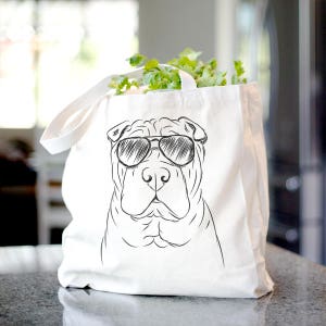 May include: A white canvas tote bag with a black and white line drawing of a Shar-Pei dog wearing sunglasses. The dog is looking directly at the viewer.