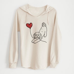 May include: A cream-colored hoodie with a V-neck and long sleeves. The front features a black line drawing of a dog reaching for a red heart-shaped balloon. The dog is drawn in a playful pose, with its paws outstretched.