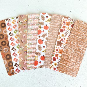 May include: A collection of colorful bookmarks with various patterns. Designs include donuts, coffee cups, cupcakes, pumpkins, autumn leaves, and coffee-themed text. The bookmarks are arranged in a fan shape.