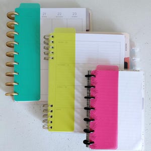 Pu&ograve; includere: Un assortimento di agende colorate con rilegatura a spirale. Le agende sono nelle tonalit&agrave; di verde acqua, giallo e rosa, con accenti oro e neri. Le pagine sono a righe e includono layout di calendario.