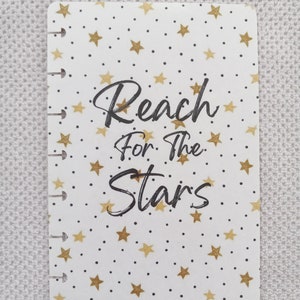 May include: White planner cover with a gold star pattern and the text "Reach for the Stars" in black.