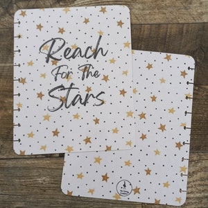 May include: Two white pages with a gold star pattern and black dots. The top page has the text "Reach for the Stars" in black cursive writing. The bottom page has a small black and white logo that says "Star Sized Creations".