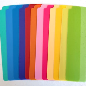 Pu&ograve; includere: Una collezione di divisori in plastica rettangolari colorati. I divisori sono disposti verticalmente, mostrando sfumature di verde, blu, rosso, arancione, rosa e giallo. Ogni divisore ha una parte superiore dentellata, su uno sfondo bianco.
