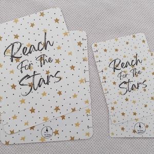 May include: Two white cardstock covers with gold stars and black text that reads "Reach for the Stars". The covers are for a disc bound planner.