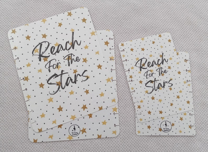 May include: Two white cardstock covers with gold stars and black text that reads "Reach for the Stars". The covers are for a disc bound planner.