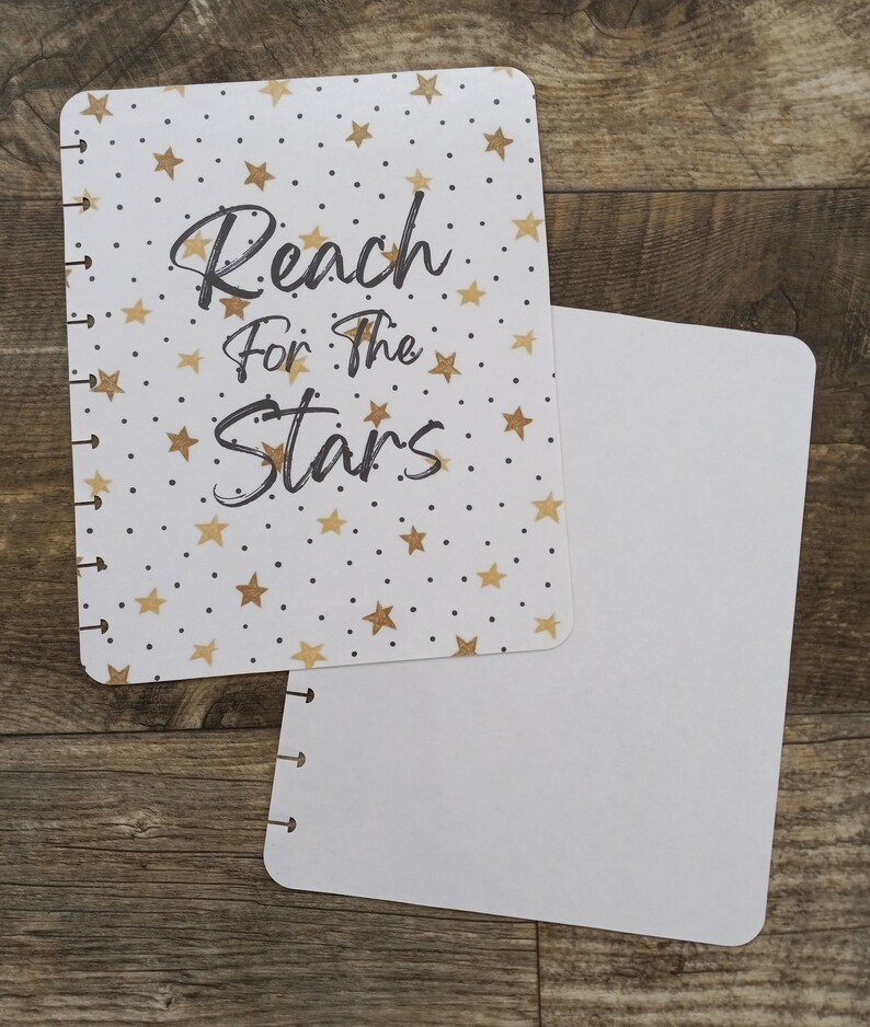 May include: A white planner with a gold star pattern and the text "Reach for the Stars". The planner is open to a blank page.