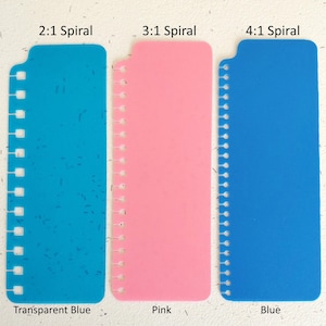 Pu&ograve; includere: Tre strumenti di rilegatura in plastica blu e rosa. Gli strumenti sono etichettati con il testo "2:1 Spiral", "3:1 Spiral" e "4:1 Spiral". I colori sono blu trasparente, rosa e blu. &Egrave; visibile anche il testo "Transparent Blue", "Pink" e "Blue".