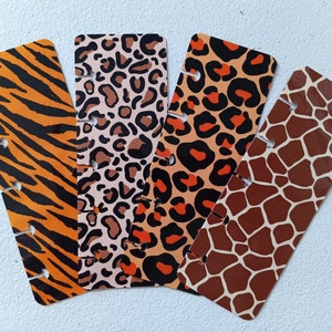 May include: Four colorful bookmarks with different animal print designs. The bookmarks are orange, black, brown, and white with tiger, leopard, giraffe, and cheetah patterns.